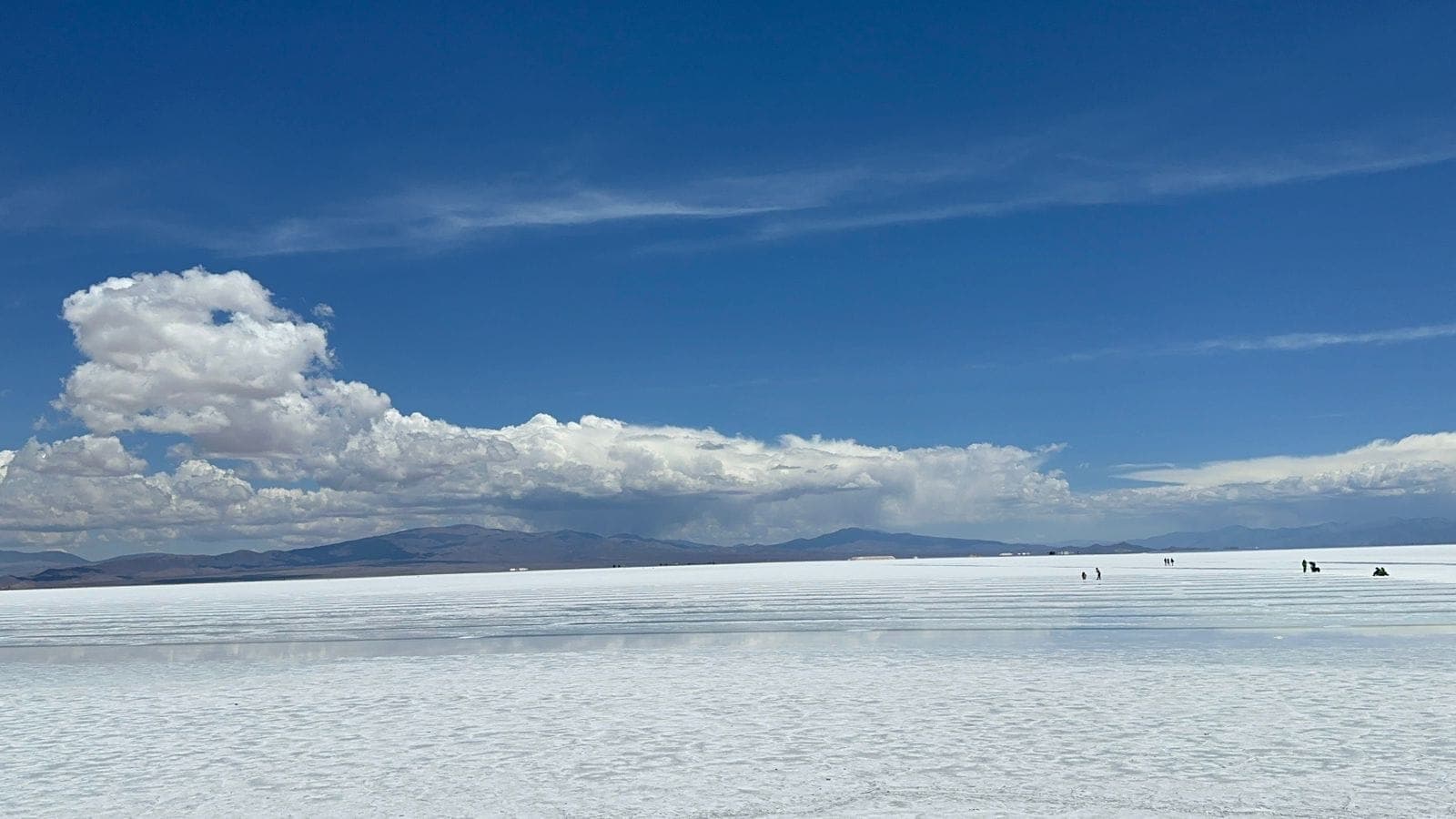 Salar branco e plano até o horizonte, sob céu azul com nuvens