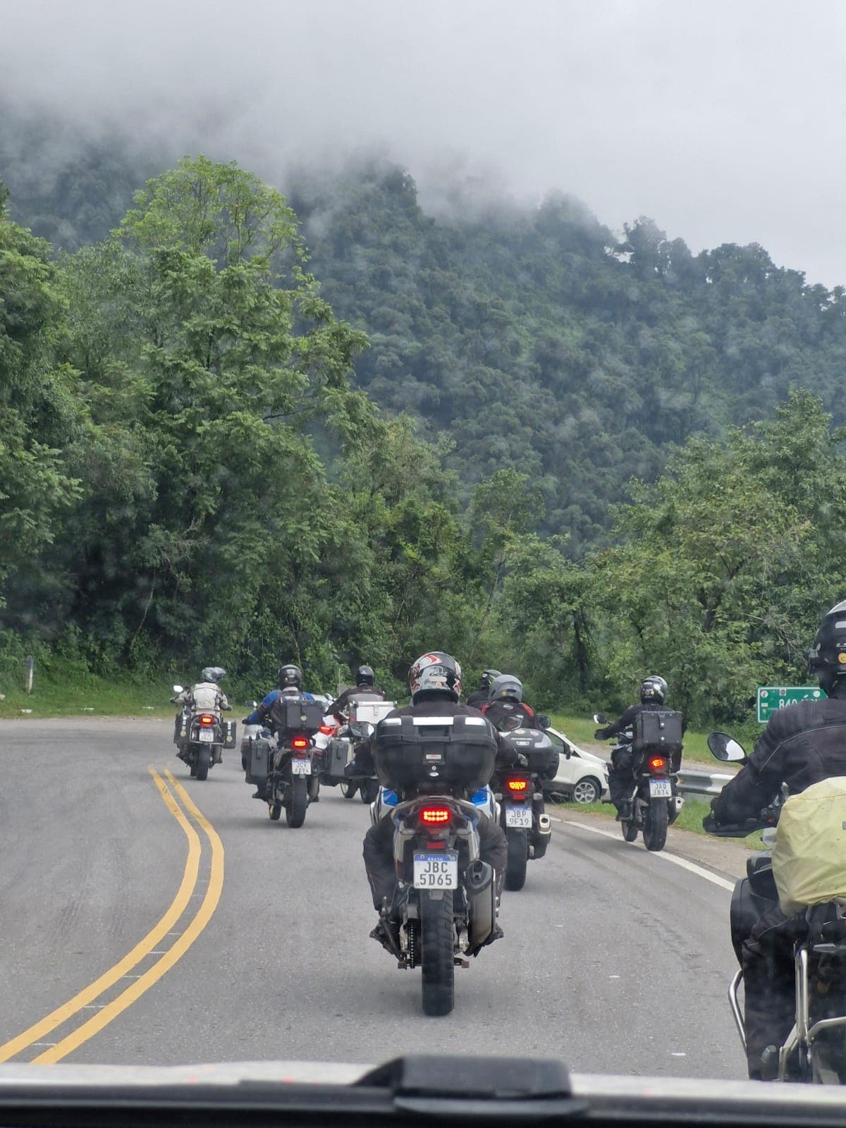 Grupo de motos numa curva de estrada de serra, entre morros cobertos de mata verde