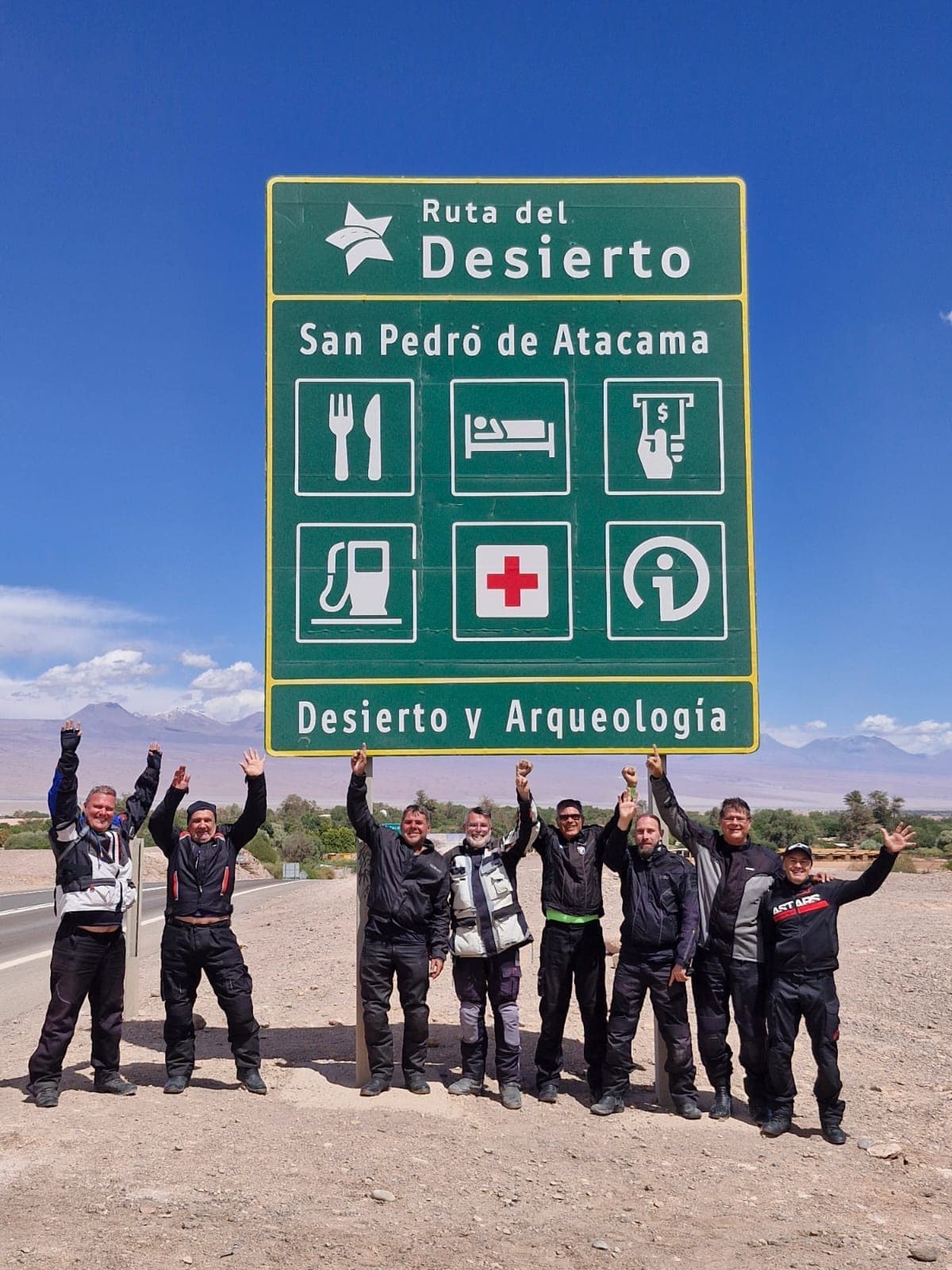 Grupo de braços erguidos sob a placa verde da Ruta del Desierto, a caminho de San Pedro de Atacama
