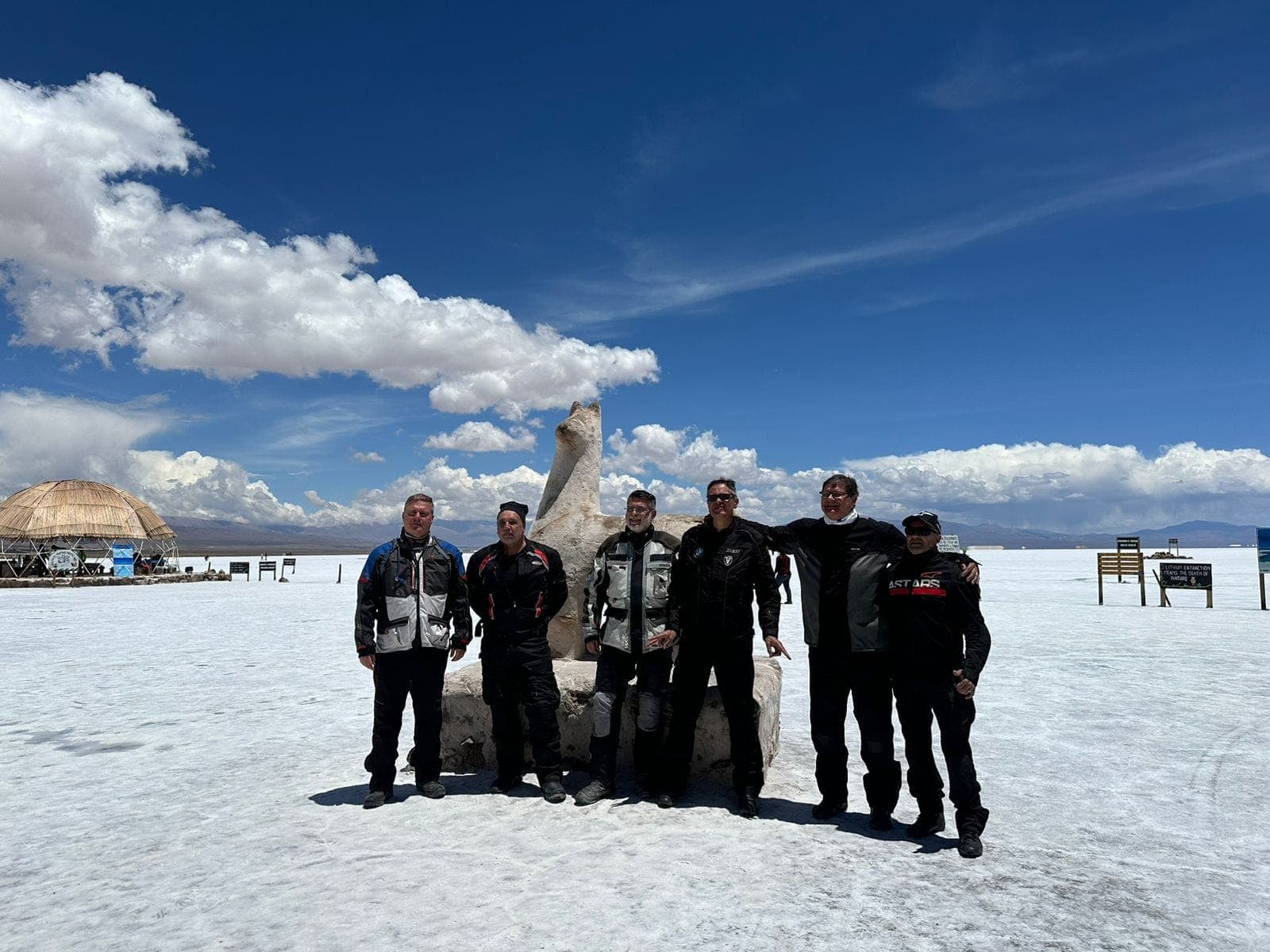 Grupo de motociclistas posando no salar branco, com céu azul e nuvens