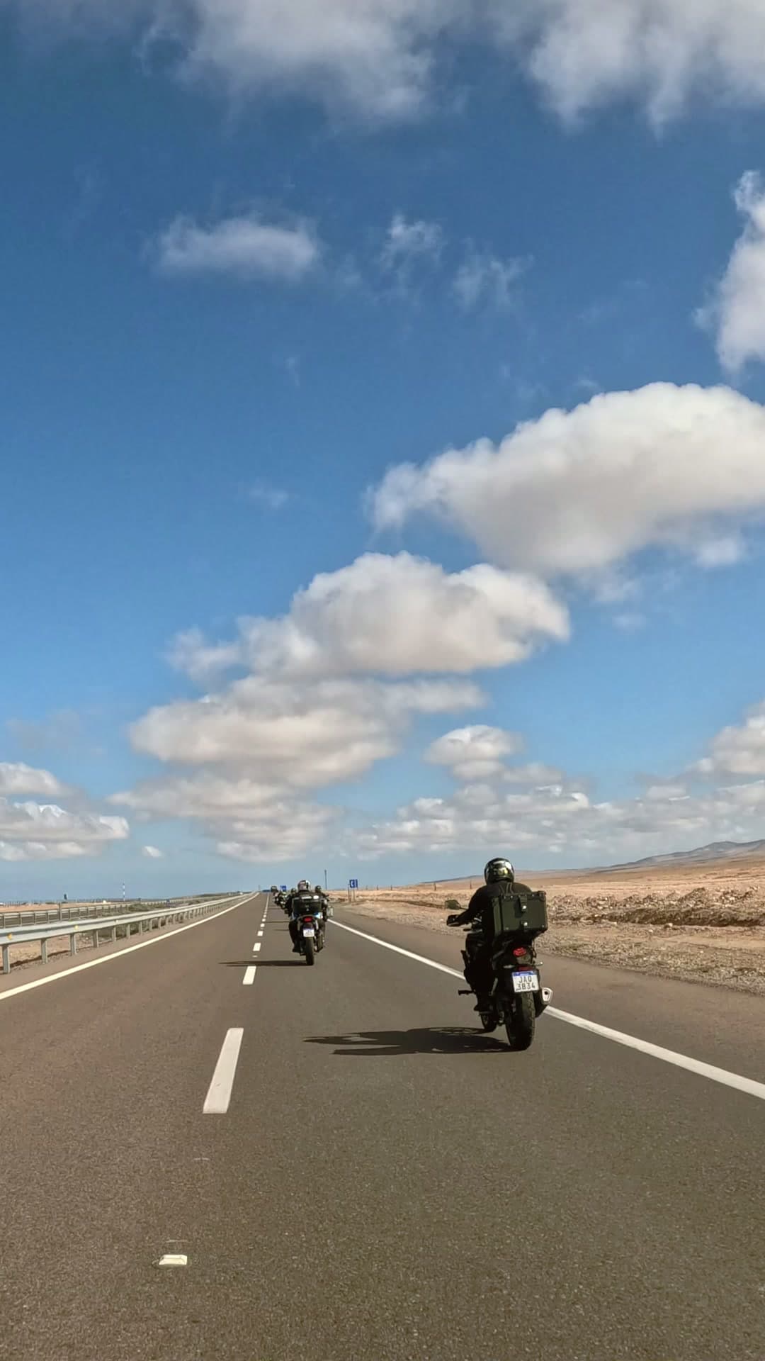 Motos em fila numa reta do deserto, sob céu azul com nuvens
